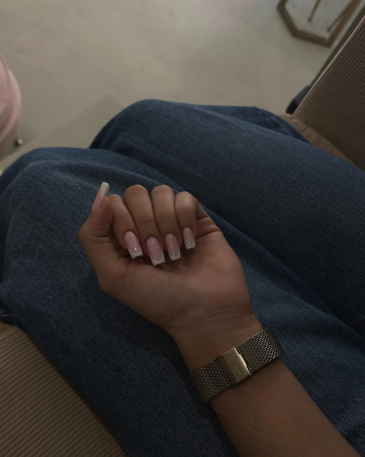 Main aux ongles carrés avec une French blanche, photographiée sur un jean.