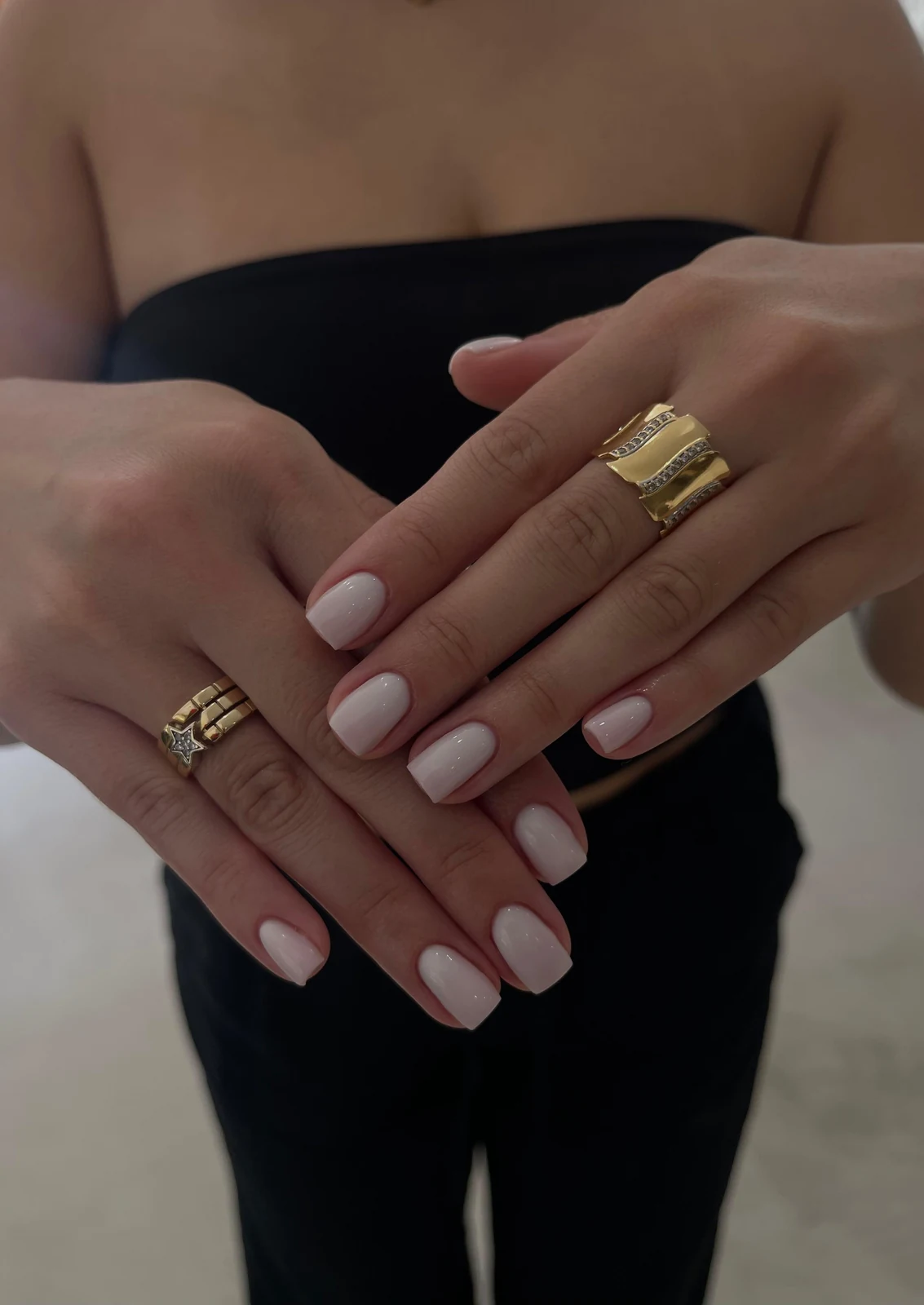 Deux mains aux ongles carrés laqués nude rosé, avec des bijoux dorés.