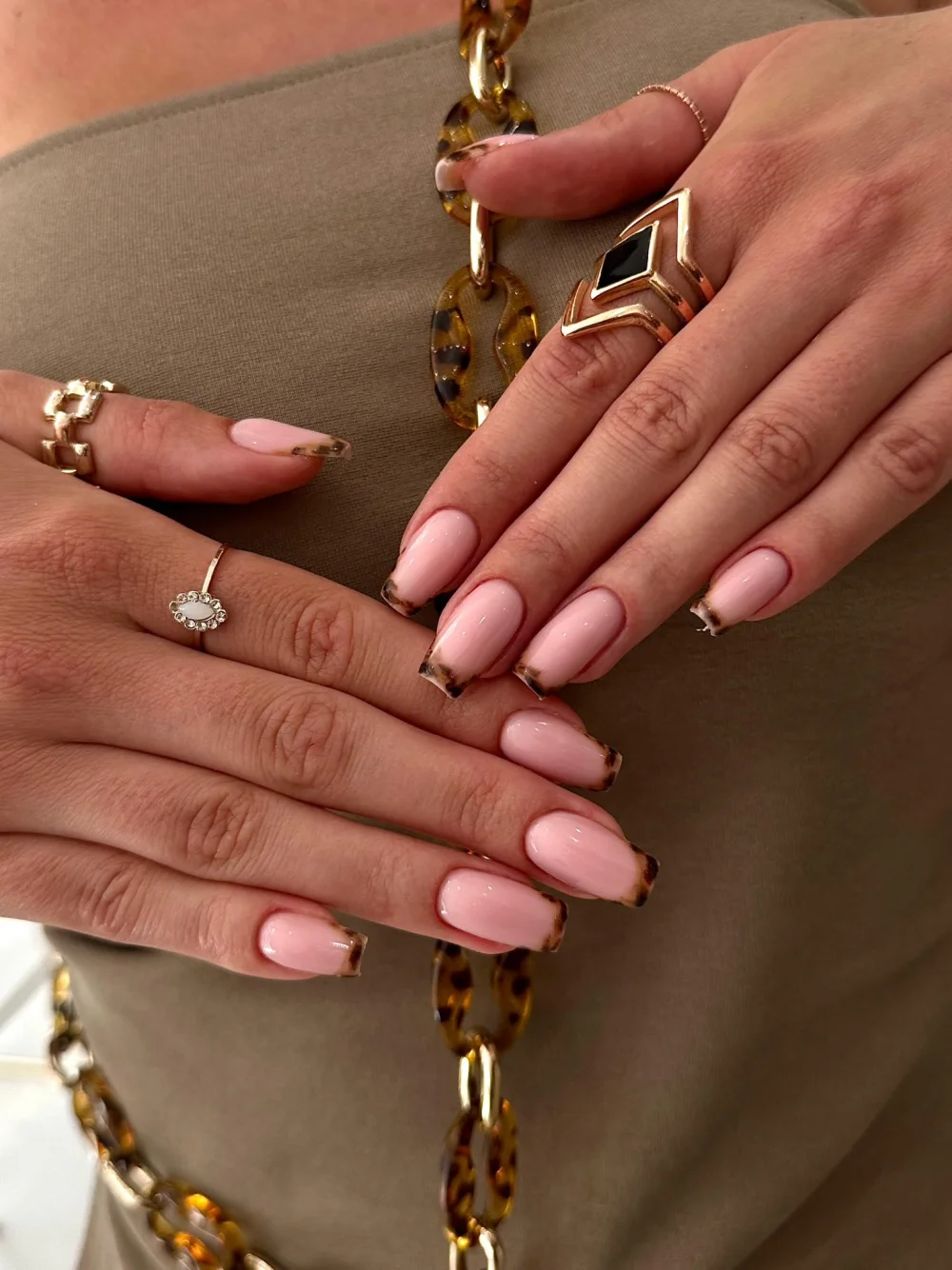 Deux mains aux ongles roses arrondis, avec une fine finition dorée.