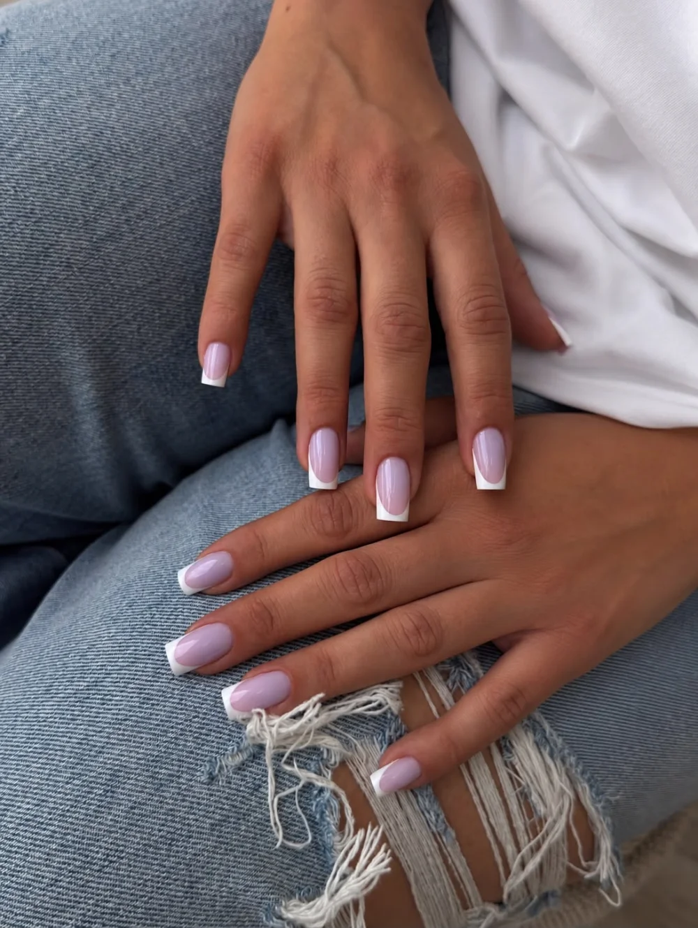 Deux mains avec une French blanche sur base rose, sur un jean.