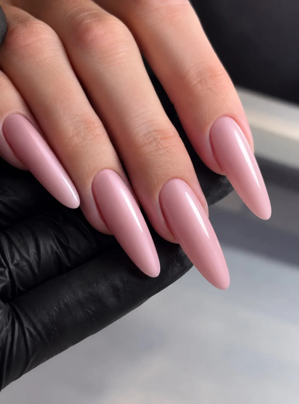 Ongles longs en amande, rose uni, photographiés sur un gant noir.